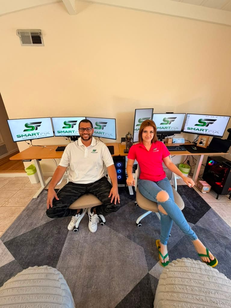 Two people sitting at a desk with multiple monitors displaying the SmartFix Appliance Repair logo.